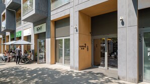 Um edifício moderno com vitrine, mesas ao ar livre e uma placa com 'SPON'.