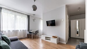 Uma sala de estar moderna com sofá, mesa de jantar, televisão fixada na parede e piso de madeira.