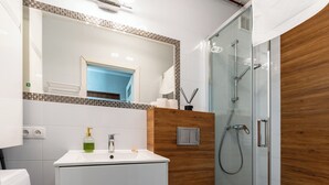 Uma casa de banho moderna com lavatório branco, toucador de madeira e cabine de duche em vidro.