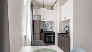 Uma cozinha compacta com armários brancos, fogão preto e painel de azulejos.