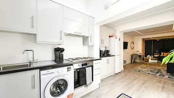 A modern kitchen with white cabinetry, a built-in washing machine, and a dining area with a black sofa and a coffee table.