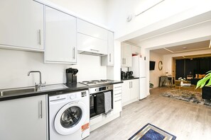 A modern kitchen with white cabinetry, a built-in washing machine, and a dining area with a black sofa and a coffee table. - Islington Garden Studio, Sleeps 4, Pet-Friendly! (Greater London)