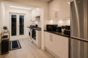 A modern kitchen with stainless steel appliances, white cabinetry, and a black countertop. - Bright N1 Studio | Tube + Garden | Sleeps 4 (Greater London)