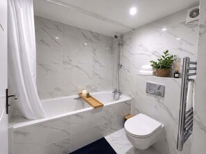 A modern bathroom with a bathtub, toilet, and shower. - Bright N1 Studio | Tube + Garden | Sleeps 4 (Greater London)