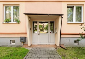 Ein Gebäudeeingang mit Doppeltüren, einem kleinen Fenster mit Pflanze und einem Gaszähler an der Wand.