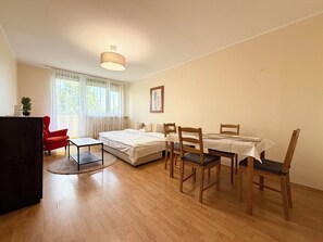 Ein Zimmer mit einem Bett, einem Schreibtisch, einem roten Sessel, einem Tisch mit Stühlen und einer Deckenleuchte.
