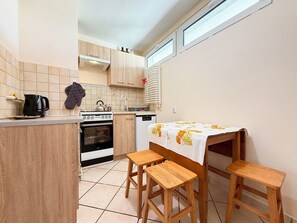 Eine kleine Küche mit Herd, Backofen und Spüle, Holzschemeln und einem Tisch mit Tischdecke.
