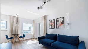 A modern living room with a blue sofa, two blue chairs, a round table, and abstract wall art. - Lasek Marceliński 12th Floor Studio (Poznań)