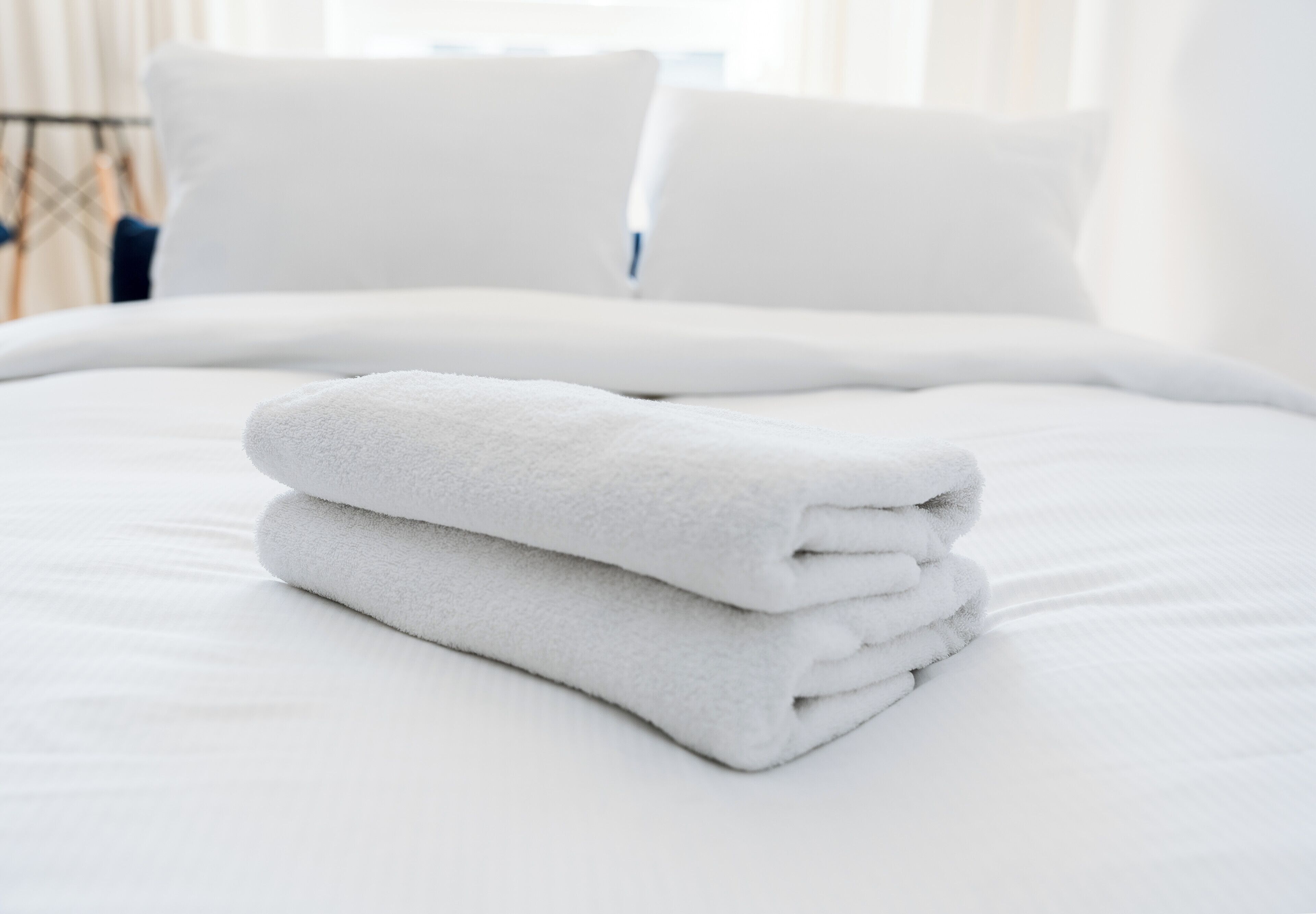 Cama bem arrumada com lençóis e almofadas brancos, disposição limpa e funcional do quarto.