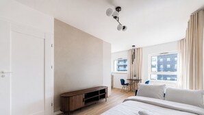 A modern hotel room with a bed, a desk, a chair, a TV stand, and a window with curtains. - Lasek Marceliński 12th Floor Studio (Poznań)