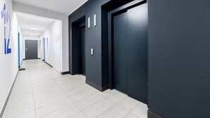A modern hallway with a dark wall, light floor tiles, and a door with a handle. - Lasek Marceliński 12th Floor Studio (Poznań)
