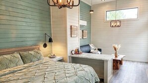 A bedroom with a bed, bedside table, lamp, and a desk with a chair. - Camp Cottonwood  (Cottonwood)