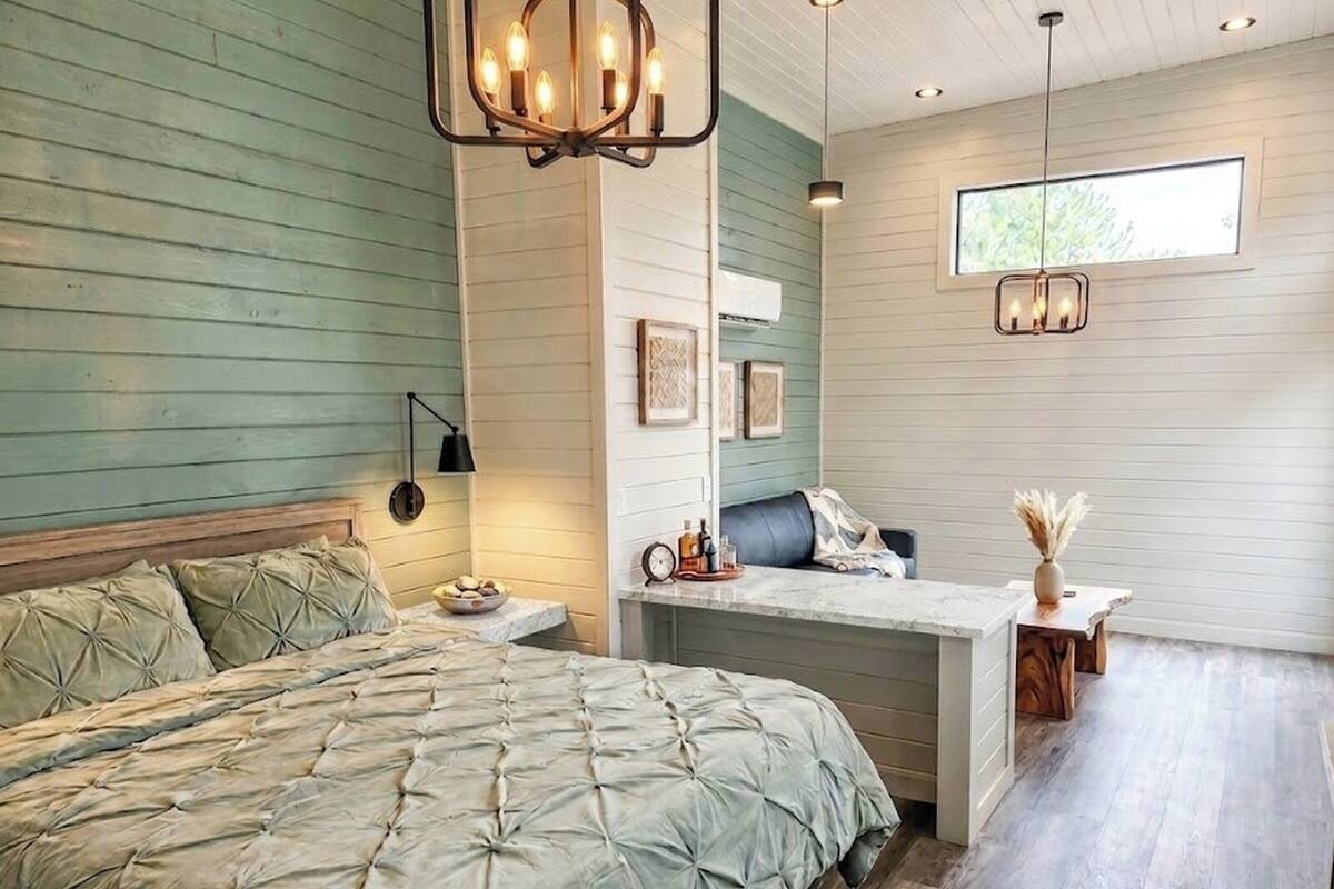 A bedroom with a bed, bedside table, lamp, and a desk with a chair.