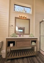 Un baño con tocador de madera, un espejo grande y una ventana sobre el lavabo.