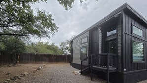 A modern cabin with a gravel driveway, a wooden deck, and a fenced yard. - Camp Cottonwood (Cottonwood)