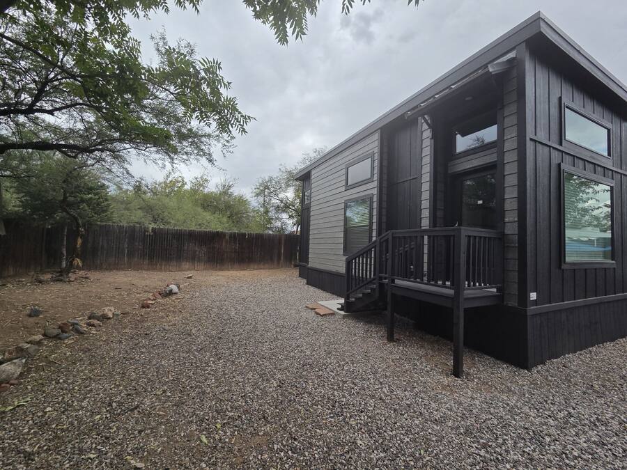 A modern cabin with a gravel driveway, a wooden deck, and a fenced yard.