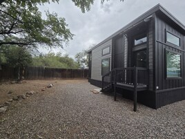Una cabaña moderna con camino de grava, terraza de madera y patio cercado.