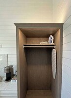Un armario pequeño de madera con repisas y espacio para colgar ropa, situado en una habitación con paneles blancos.