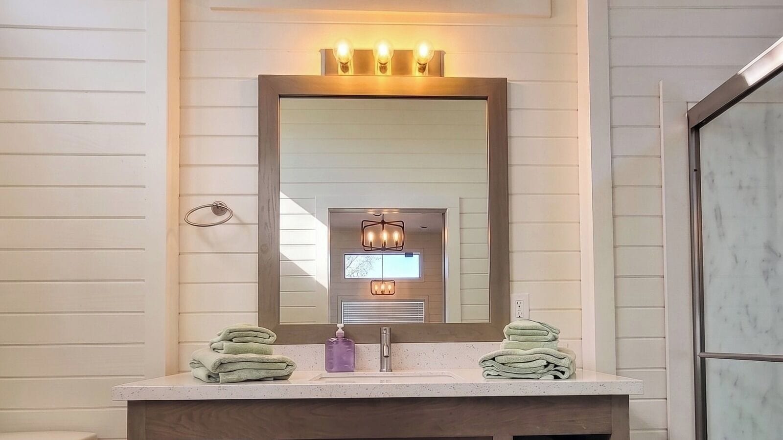 A bathroom with a wooden vanity, a large mirror, and two towel stacks.
