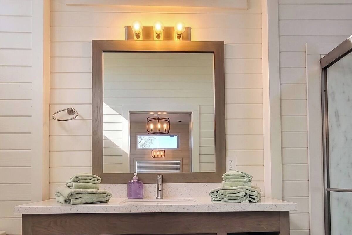 A bathroom with a wooden vanity, a large mirror, and two towel stacks.