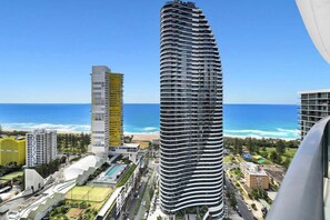 Ein modernes Hochhaus-Hotel mit geschwungener Fassade, nahe einem Strand unter blauem Himmel.