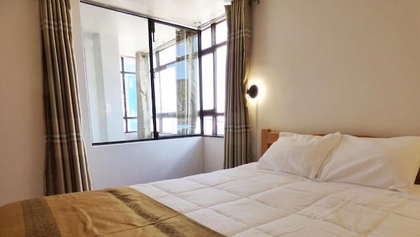 Una habitación de hotel con cama, ventana con cortinas y una lámpara fijada a la pared.