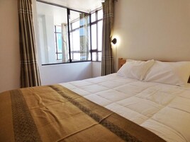 Una habitación de hotel con cama, ventana con cortinas y una lámpara fijada a la pared.