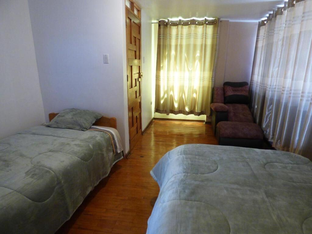 A room with two beds, a wooden wardrobe, a curtain, and a small seating area.