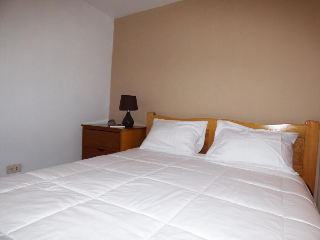 A neatly made bed with white bedding, a wooden headboard, and a small bedside table with a lamp.
