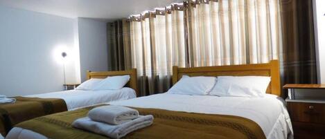 A hotel room with two beds, a wooden headboard, a nightstand, and a lamp.