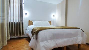 A single bed with a wooden frame, white bedding, and a brown throw blanket. There are two wall-mounted lights on either side of the bed.