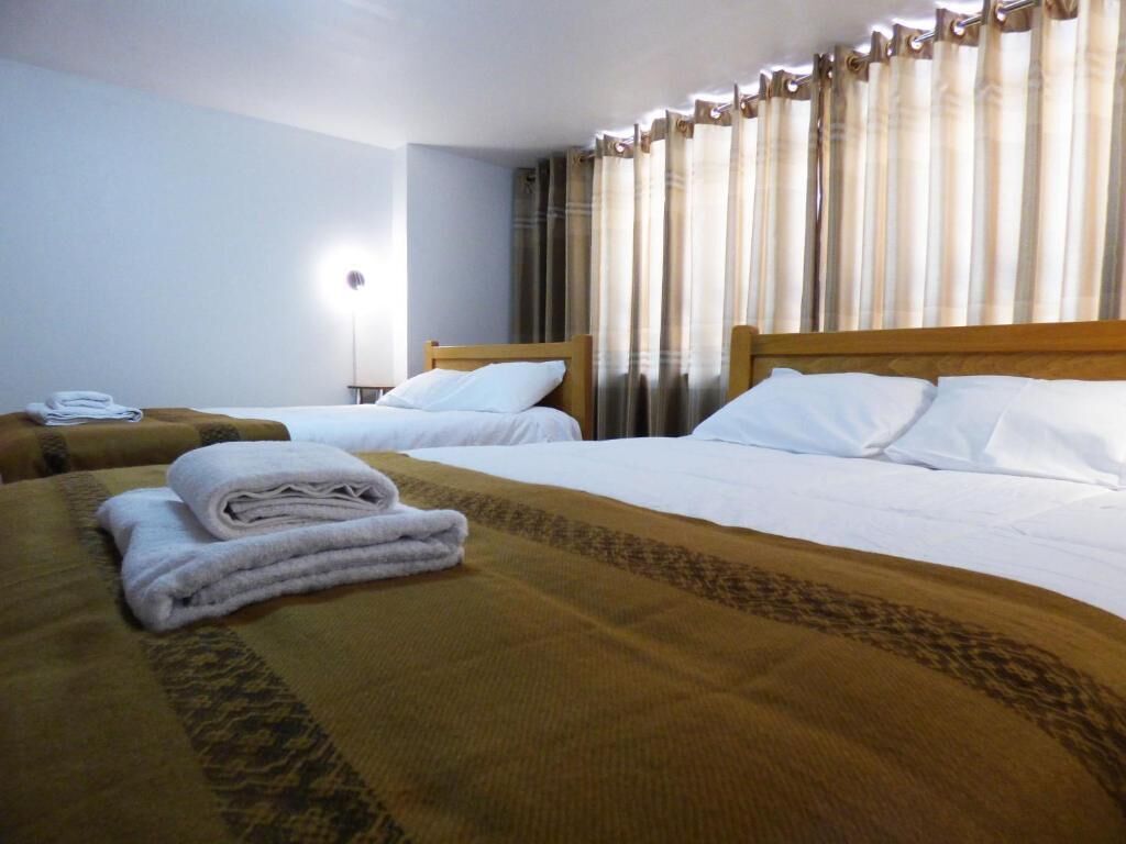 Een hotelkamer met twee bedden, een nachtkastje met een lamp en een raam met gordijnen.