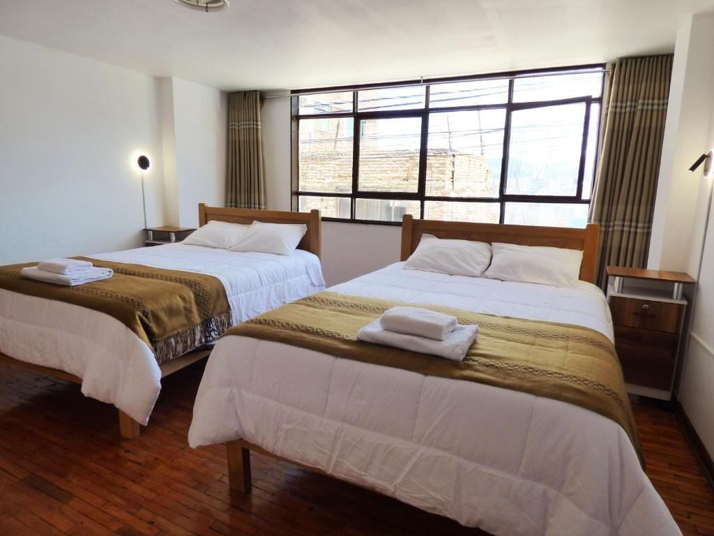 A hotel room with two beds, a large window, and a wooden floor.