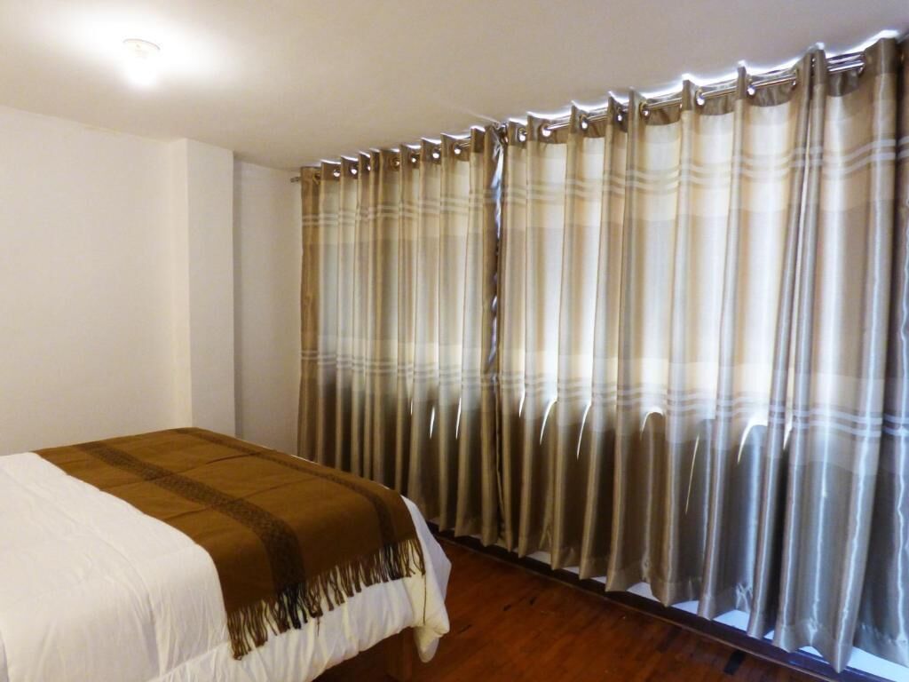 Un dormitorio con cama, cortinas y suelo de madera.