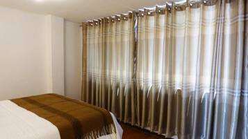 Un dormitorio con cama, cortinas y suelo de madera.