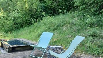 Two light blue lounge chairs on a wooden deck with a metal table, surrounded by dense greenery.