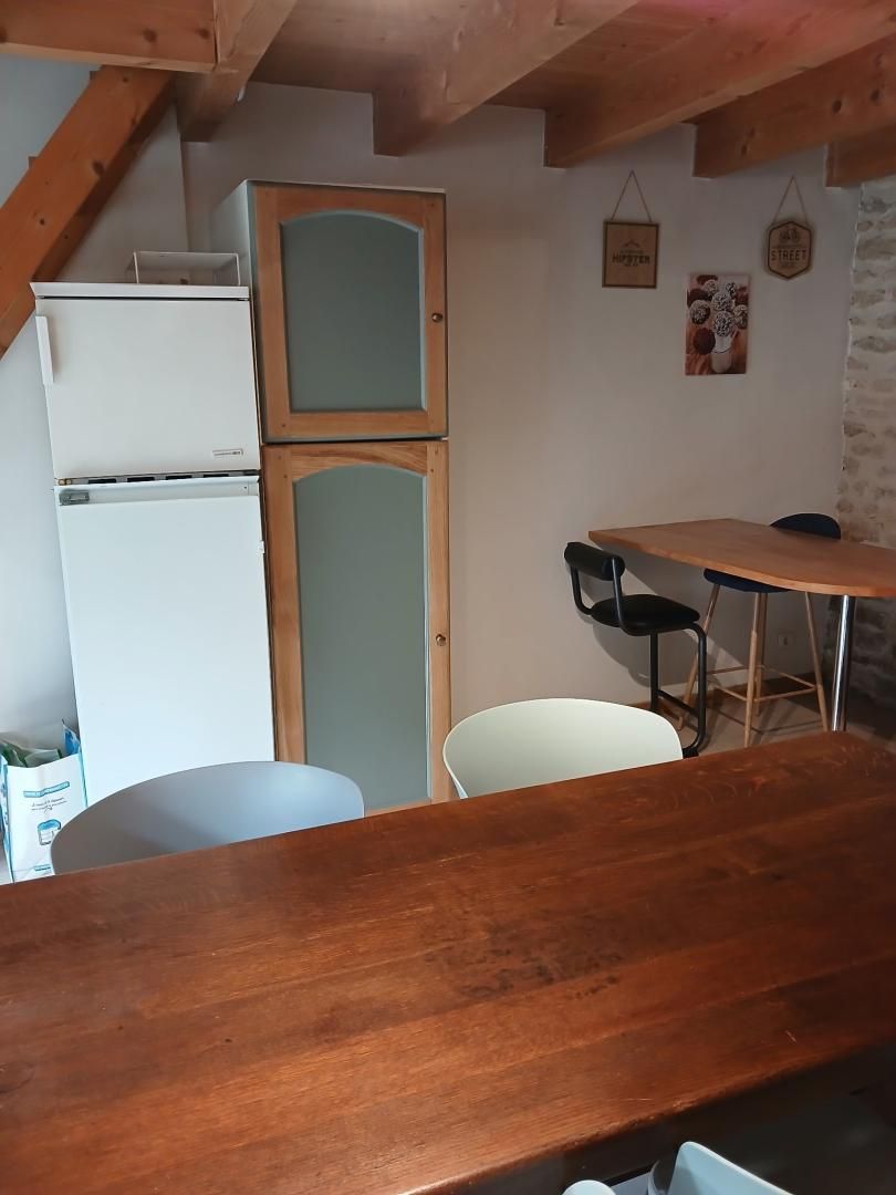 A kitchen with a wooden table, white chairs, a white refrigerator, and a wooden cabinet.