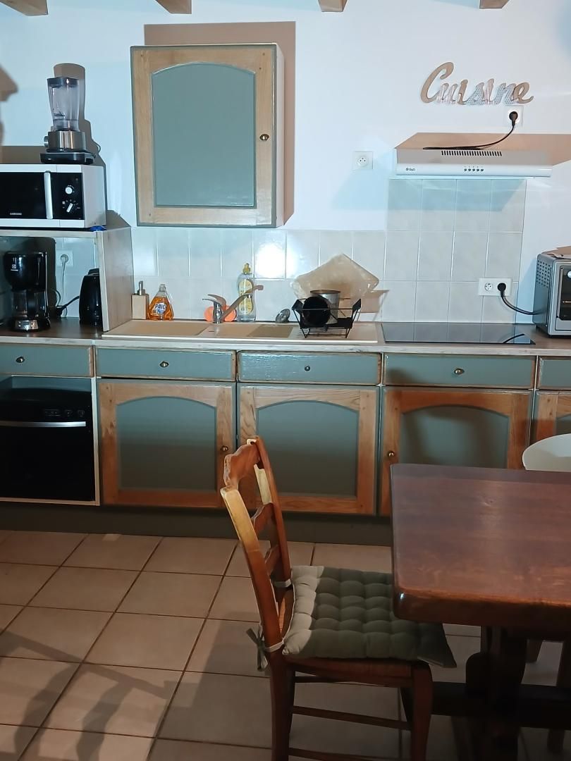 Une cuisine avec un meuble en bois, un mixeur, une machine à café, un grille-pain et une chaise.