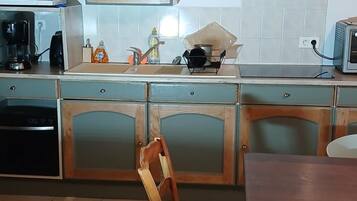 Une cuisine avec un meuble en bois, un mixeur, une machine à café, un grille-pain et une chaise.