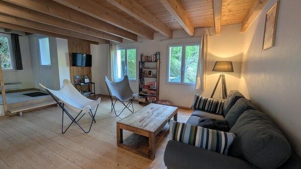 Een ruime woonkamer met houten plafond, een bank, een salontafel en een televisie.