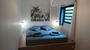 Ein Schlafzimmer mit einem Bett, einer Wandleuchte, einem Fenster mit Vorhängen und einem Wandbild.