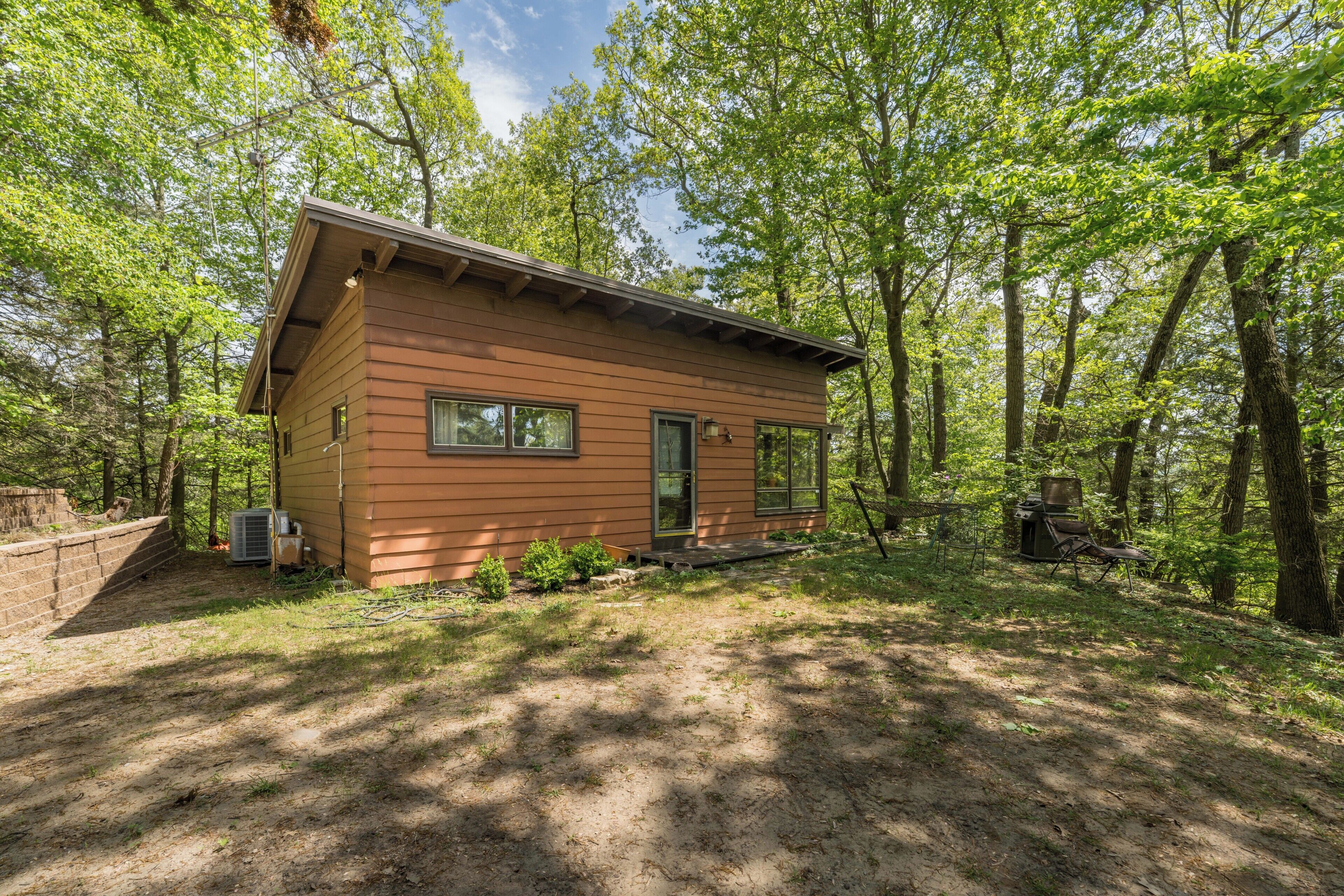 Une petite cabane avec un porche à l’avant, entourée d’arbres.