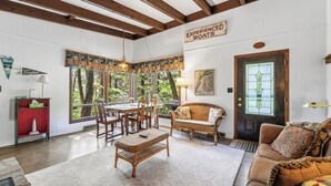 Una habitación acogedora con una mesa de comedor, sillas, un banco de mimbre, un armario rojo, un sofá de mimbre, una alfombra estampada y una puerta con un letrero.