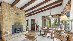 Una chimenea de piedra, vigas de techo de madera, una zona de comedor con sillas y un sofá.