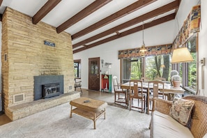 A stone fireplace, wooden ceiling beams, a dining area with chairs, and a sofa.