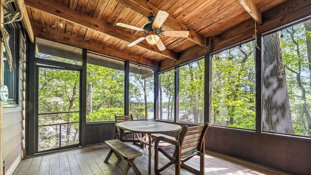 Una terraza de madera con una mesa, sillas, ventanas grandes y un ventilador de techo.