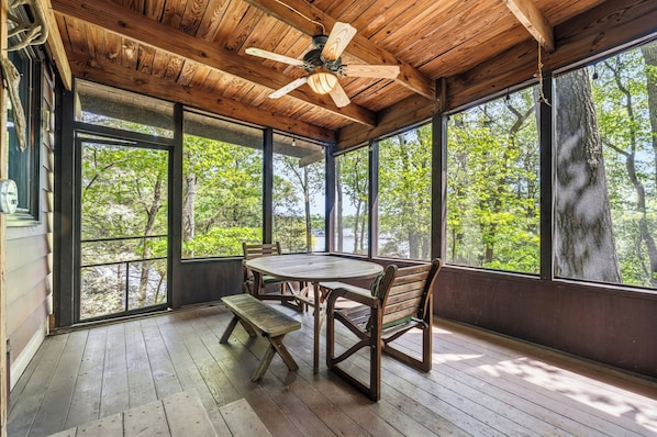 A wooden deck with a table and chairs, large windows, and a ceiling fan.