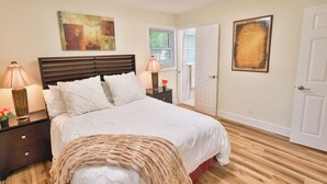 Una camera da letto con un letto, comodini, una lampada, un quadro e una porta.