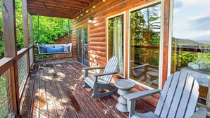 Une terrasse en bois avec des fauteuils Adirondack et une balançoire, de grandes fenêtres et une vue sur la verdure.