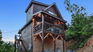 Une cabane en rondins dotée d’un balcon, d’un espace salon extérieur et d’un escalier.